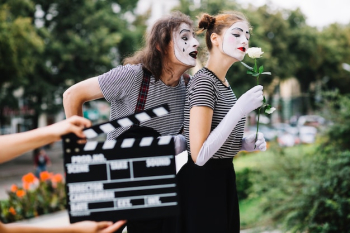 A person's hand holding clapperboard in front of mime couple
