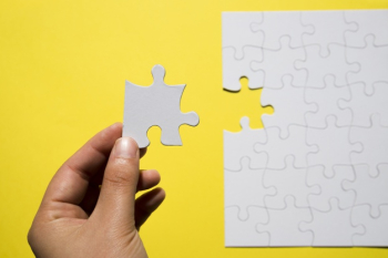 A person's hand holding missing white jigsaw puzzle piece over yellow backdrop Free Photo