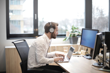  A young caucasian man working on laptop while wearing headset 