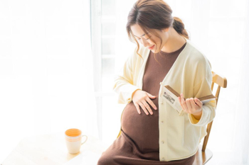 A young happy pregnant woman is reading a book and drinking tea while relaxing on the chair