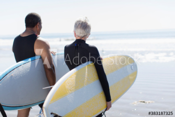 Active senior couple carrying surfboards on sunny beach Active senior couple carrying surfboards on sunny beach