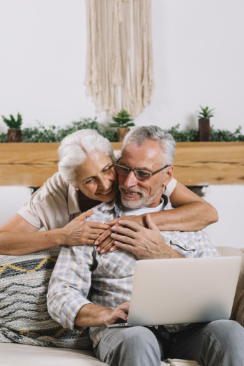 An elderly woman embracing her husband using laptop An elderly woman embracing her husband using laptop