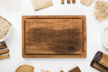 An overhead view of empty wooden tray with spatula; rice; cinnamon sticks on white background