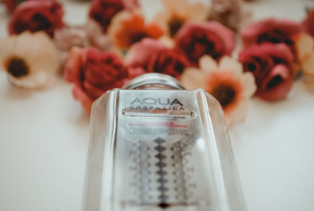 Aqua Carpalica Bottle Near Flowers on White Surface