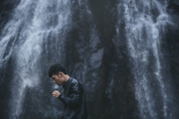 Asian man standing in front of the waterfall Asian man standing in front of the waterfall