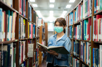 Asian university student girl wearing face protective medical mask for protection from virus disease reading book at library. Education, high school, university, learning and people concept