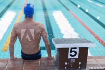 Athletic male swimmer sitting at edge of swimming pool