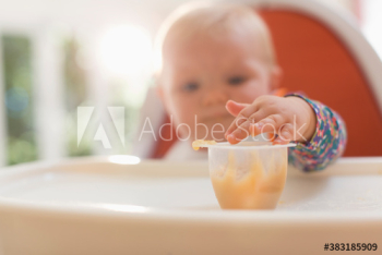 Baby girl in high chair reaching for baby food Baby girl in high chair reaching for baby food