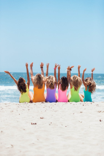 Back view photo of six girls wearing swimsuit sitting on white sand Back view photo of six girls wearing swimsuit sitting on white sand