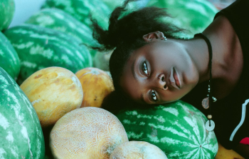 Beautiful conceptual portrait of a black model posing with her head on melons and water melons.