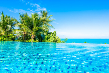 Beautiful luxury outdoor swimming pool in hotel resort with sea ocean around coconut palm tree and white cloud on blue sky Free Photo
