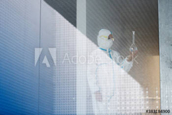 Biochemist in clean suit examining beaker with liquid Biochemist in clean suit examining beaker with liquid