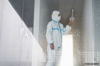 Biochemist in clean suit examining beaker with liquid in laboratory Biochemist in clean suit examining beaker with liquid in laboratory