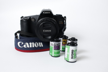 Black Canon Eos Camera Beside Four Camera Films On White Surface