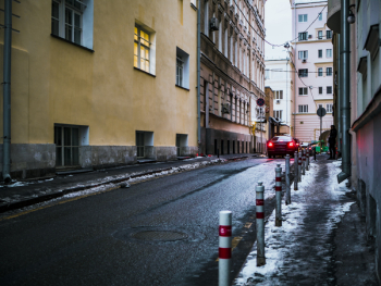 Black Car Crossing Asphalt Road Between Buildings