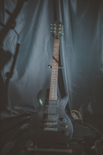 Black Electric Guitar on Guitar Stand in Front Black Garment Black Electric Guitar on Guitar Stand in Front Black Garment