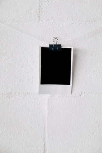 Blank polaroid photo on string attach with bulldog paper clips against white wall
