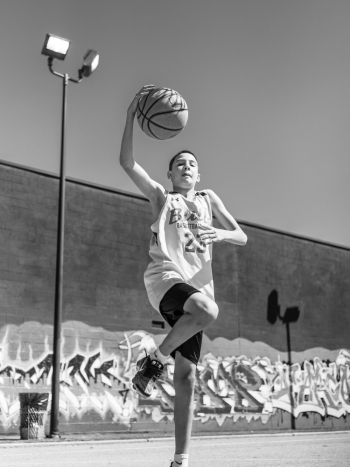 Boy Standing on One Leg Holding Basketball Outdoors Boy Standing on One Leg Holding Basketball Outdoors