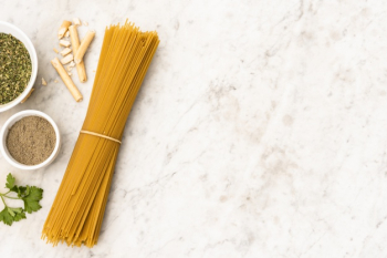 Bundle of uncooked spaghetti pasta and ingredient on marble textured background Free Photo