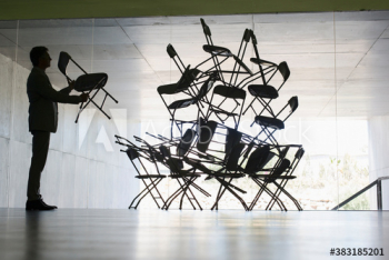 Businessman stacking chairs in office Businessman stacking chairs in office