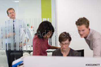 Businessman watching colleagues at computer in office Businessman watching colleagues at computer in office