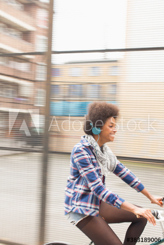 Carefree young woman with headphones riding bicycle on sidewalk