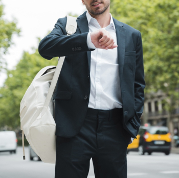 Close-up of a businessman with white backpack on his shoulder watching time on street Free Photo