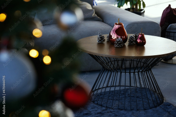 Close up of modern small round wooden table with beautiful decoration near cozy grey sofa and near Christmas tree. Concept of modern fashionable interior with Christmas decoration.
