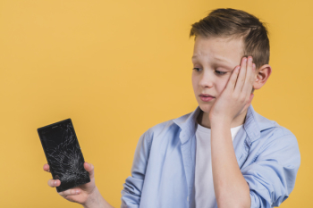 Close-up of upset boy looking at broken screen of mobile phone against yellow background