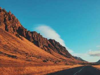 concrete road beside mountain under blue sky concrete road beside mountain under blue sky