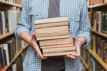 Crop teenager with books between bookshelves Crop teenager with books between bookshelves