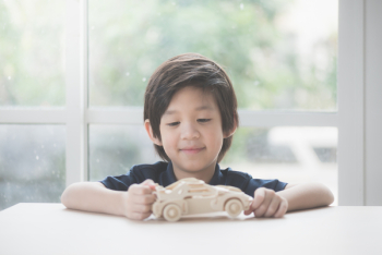 Cute Asian child playing wooden model car on a table