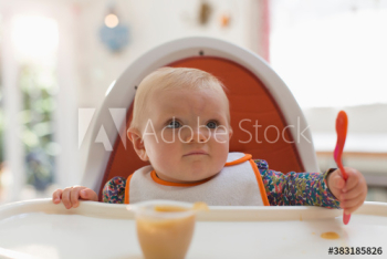 Cute baby girl eating baby food in high chair Cute baby girl eating baby food in high chair