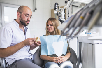 Dentist working on dental jaw near female patient sitting on dental chair