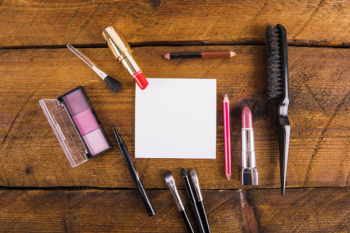 Elevated view of cosmetic products with hairbrush and blank paper on wooden background