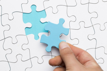 Elevated view of hand holding blue puzzle piece over white puzzle background Free Photo