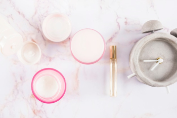 Elevated view of moisturizing creams; perfume and alarm clock on marble