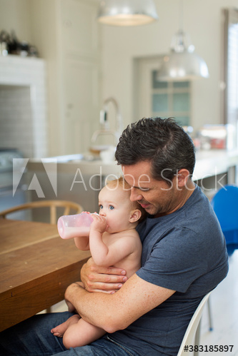 Father holding baby son with baby bottle at dining table Father holding baby son with baby bottle at dining table