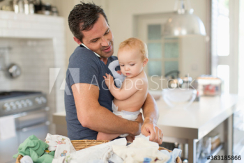 Father multitasking holding baby son and folding laundry Father multitasking holding baby son and folding laundry