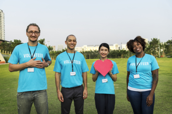 Four Smiling People Standing On Green Grass