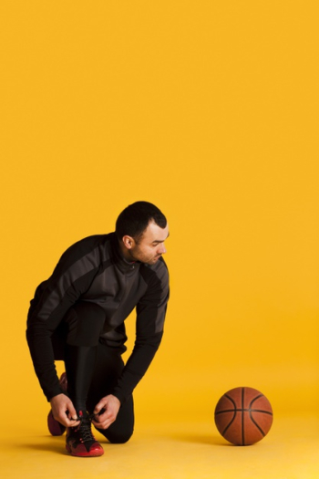 Front view of male basketball player tying shoe laces with ball and copy space Free Photo