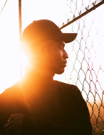 golden hour photography of man standing beside cyclone fence