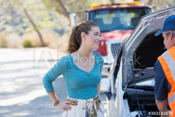 Grateful woman watching male roadside assistance mechanic fix car