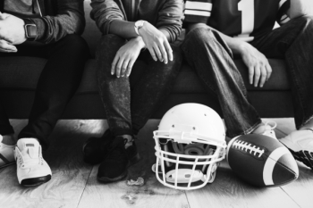 Grayscale Football Helmet on Floor and Man Sit on Sofa Grayscale Football Helmet on Floor and Man Sit on Sofa