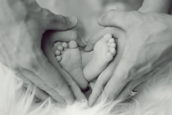 Grayscale Photo of Baby Feet With Father and Mother Hands in Heart Signs
