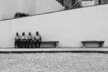 Grayscale Photo of Four Men Sitting on Bench Along the Street
