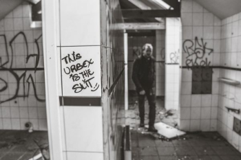 grayscale photo of man standing near white tile wall grayscale photo of man standing near white tile wall