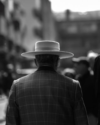 grayscale photo of man wearing hat standing beside building grayscale photo of man wearing hat standing beside building