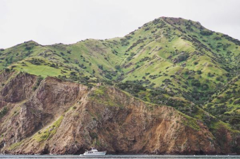 green mountain near body of water with white watercraft during daytime