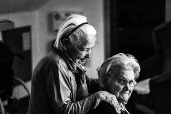 greyscale photo of woman standing behind woman sitting on chair greyscale photo of woman standing behind woman sitting on chair
